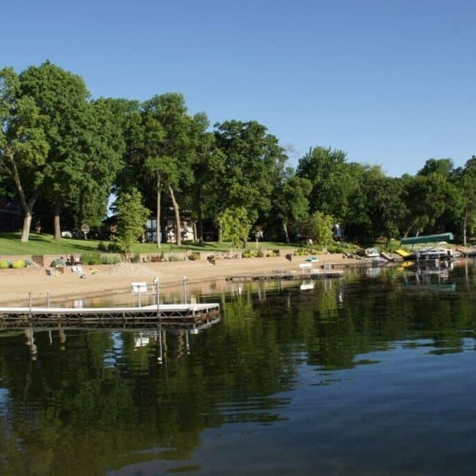 Docks and beach area on lake with trees in background.